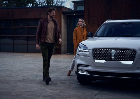 A man and a woman approaching a 2024 Lincoln Aviator® SUV, which illuminates certain lights when they are close | LaFontaine Lincoln Grand Rapids in Grand Rapids MI
