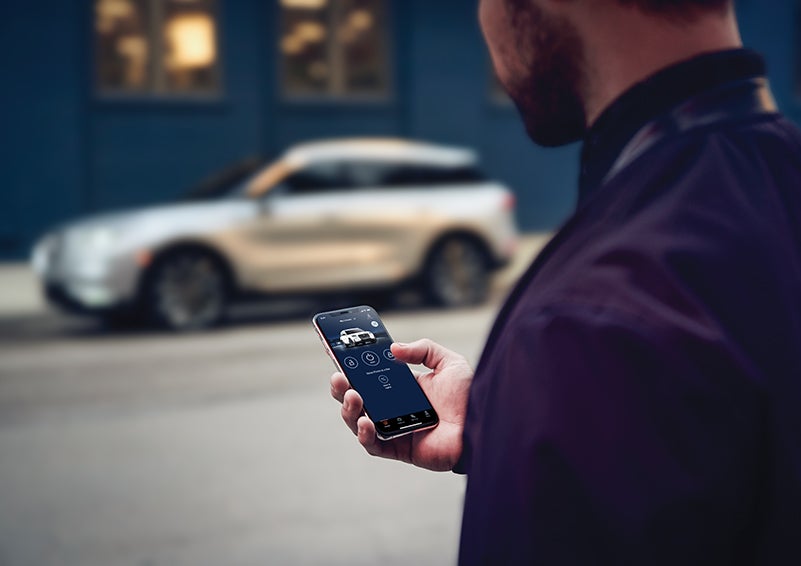 A person is shown interacting with a smartphone to connect to a Lincoln vehicle across the street. | LaFontaine Lincoln Grand Rapids in Grand Rapids MI