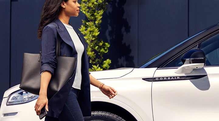 A woman approaches a 2024 Lincoln Corsair® SUV while holding a smartphone. | LaFontaine Lincoln Grand Rapids in Grand Rapids MI