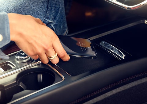 A smartphone is is being placed on the wireless charging pad in the front center console cubby. | LaFontaine Lincoln Grand Rapids in Grand Rapids MI