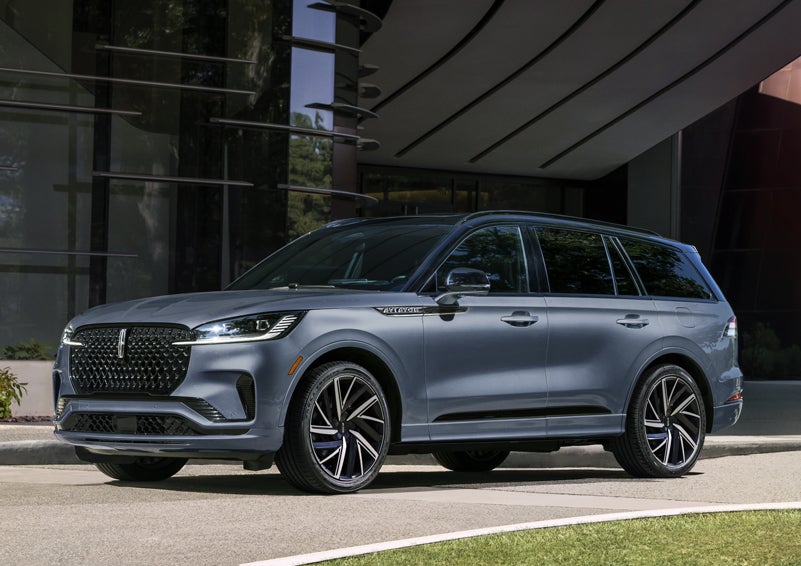 A gray 2025 Lincoln Aviator® SUV is parked outside a modern building showcasing the driver’s side of the vehicle. | LaFontaine Lincoln Grand Rapids in Grand Rapids MI