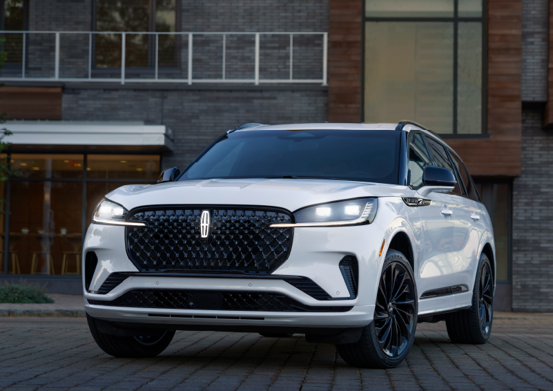 A white 2025 Lincoln Aviator® SUV is shown parked outside a modern building with gray brick and wood accents. | LaFontaine Lincoln Grand Rapids in Grand Rapids MI