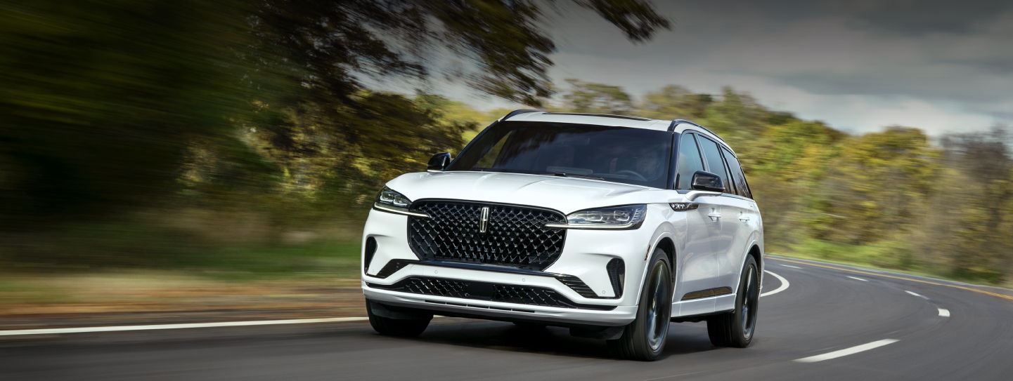 A white 2025 Lincoln Aviator® SUV is being driven down a road lined with trees. | LaFontaine Lincoln Grand Rapids in Grand Rapids MI