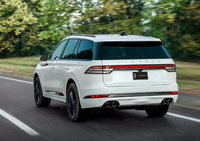A white 2026 Lincoln Aviator® SUV is being driven away down a road lined with colorful trees. | LaFontaine Lincoln Grand Rapids in Grand Rapids MI