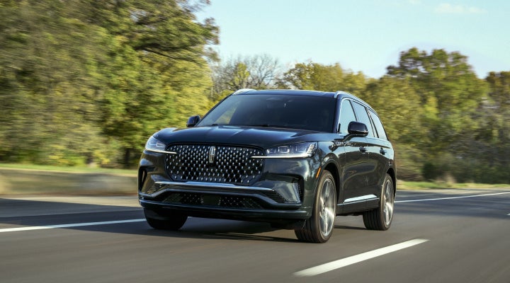 A 2026 Lincoln Black Label™ Aviator® SUV is being driven down a road lined with trees. | LaFontaine Lincoln Grand Rapids in Grand Rapids MI