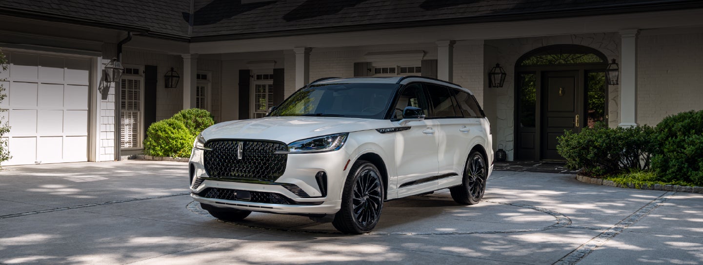 A white 2026 Lincoln Aviator® SUV is parked in the driveway of a luxury home. | LaFontaine Lincoln Grand Rapids in Grand Rapids MI