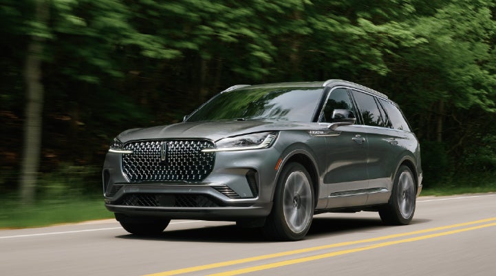 A 2027 Lincoln Aviator® SUV is being driven down a road lined with trees. | LaFontaine Lincoln Grand Rapids in Grand Rapids MI