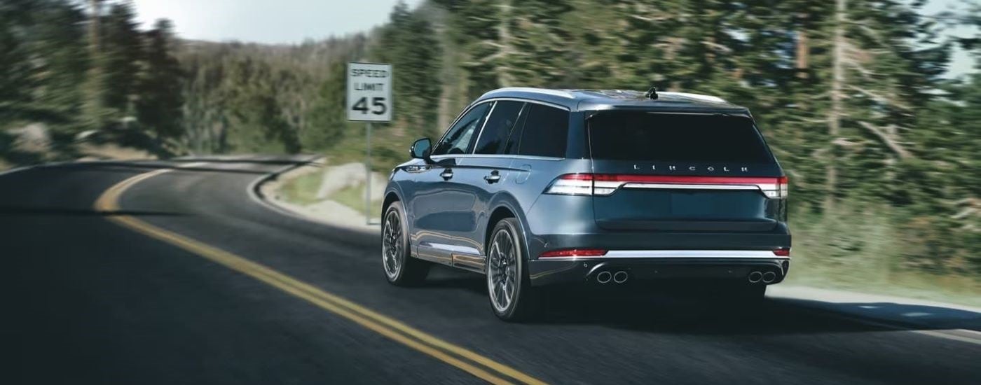 Rear of a blue 2023 Lincoln Aviator driving down a winding road.