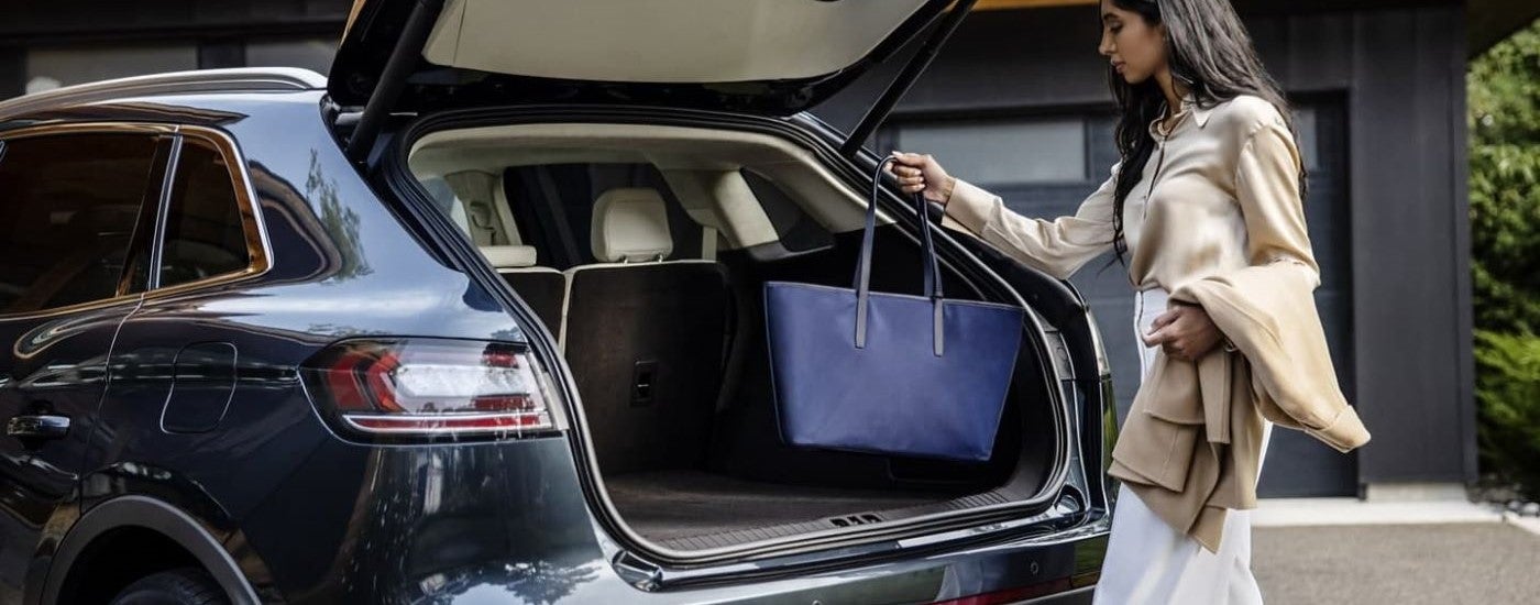 A person stowing a bag inside of a blue 2023 Lincoln Nautilus.