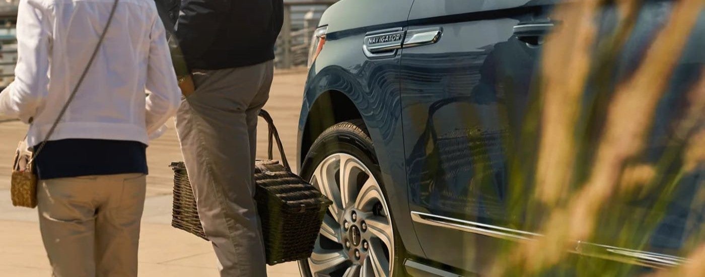 Two people walking nearby a blue 2023 Lincoln Navigator.