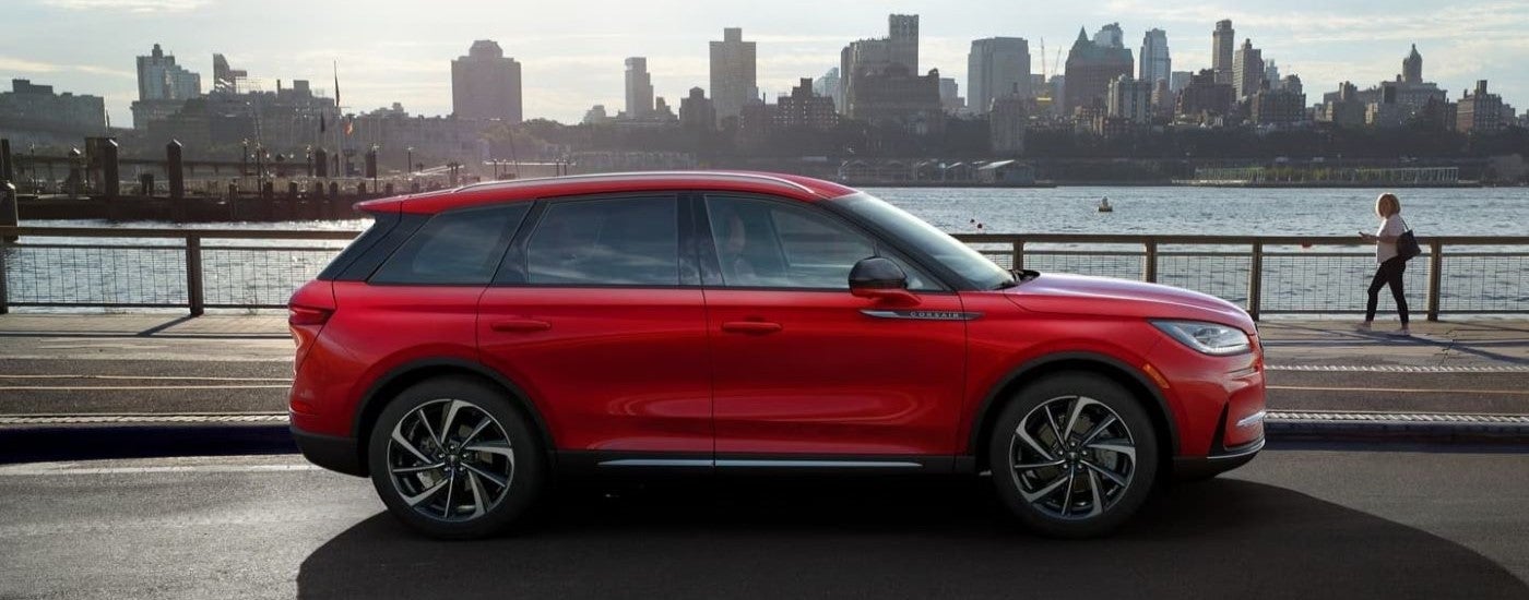 Side view of a red 2024 Lincoln Corsair driving past a city